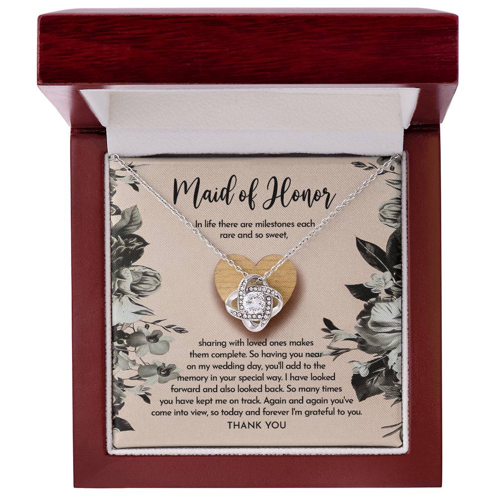 The "To Maid of Honor, My Wedding Day - Love Knot Necklace" features a heart-shaped pendant on a card titled "Maid of Honor," with a heartfelt message about milestones, love, and gratitude. The pendant is available in white gold or yellow gold finish and is adorned with sparkling cubic zirconia crystals.