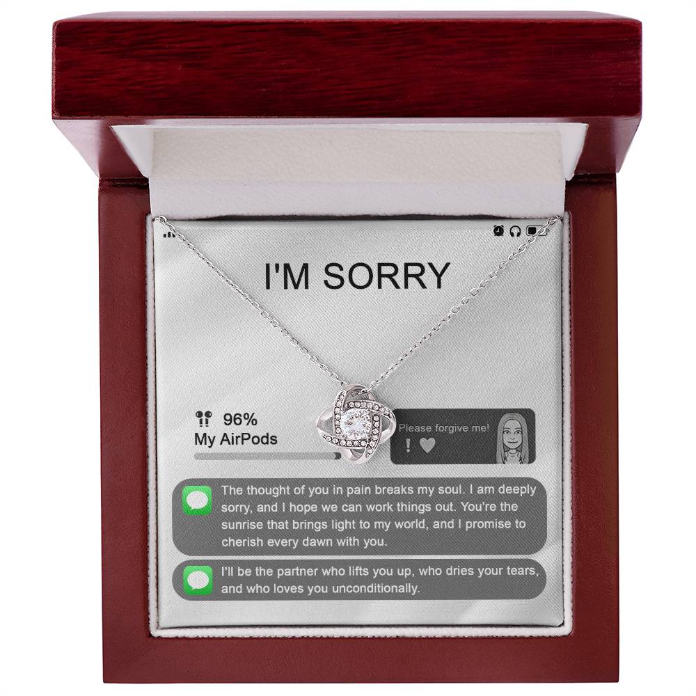 The "Sorry-Breaks My Soul - Love Knot Necklace" is a silver necklace featuring a pendant, beautifully displayed in its packaging. The front of the packaging includes a heartfelt apology message, text messages, a battery icon showing 96% for AirPods, and an illustrated figure. This intricately crafted piece is made from 14k white gold and adorned with cubic zirconia crystals.