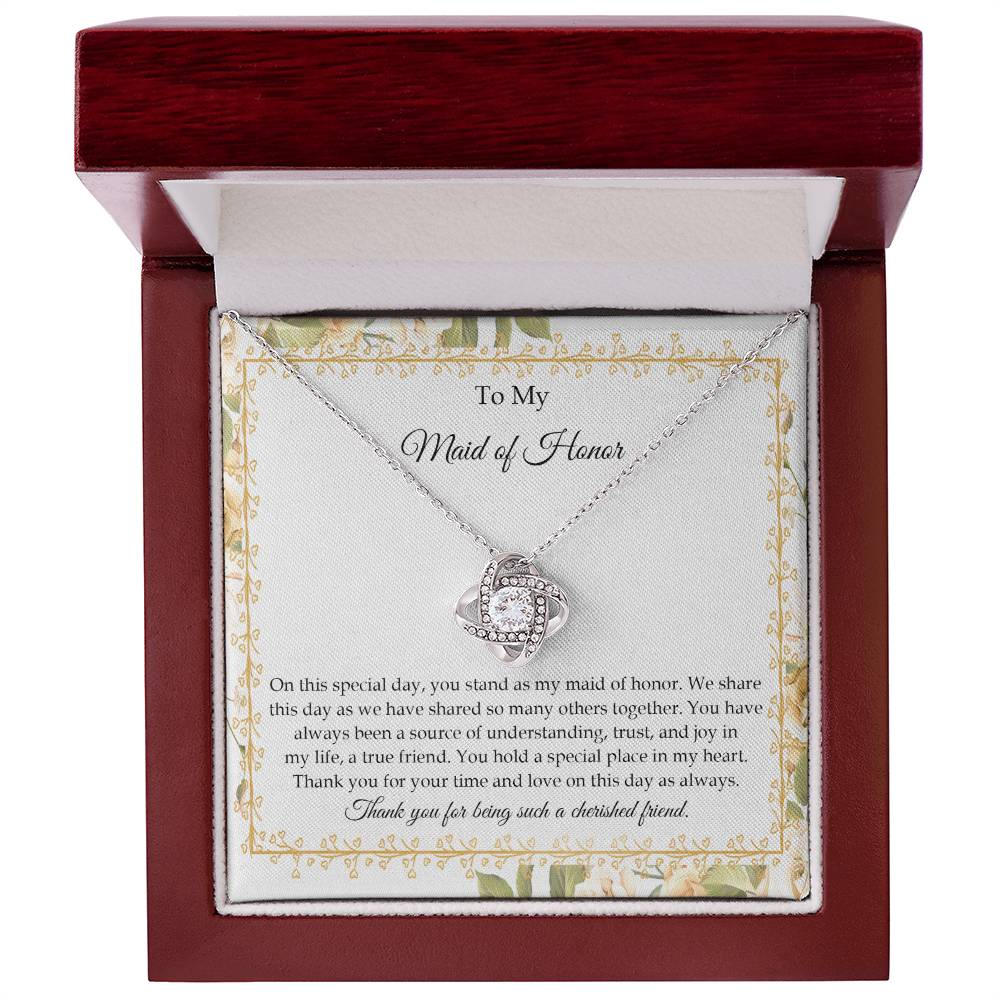 Presenting the "To Maid of Honor, Share This Day - Love Knot Necklace," featuring a stunning pendant adorned with cubic zirconia crystals and finished in white gold. It is beautifully displayed in a box embellished with a floral border and includes a heartfelt message expressing gratitude and appreciation to the "Maid of Honor.