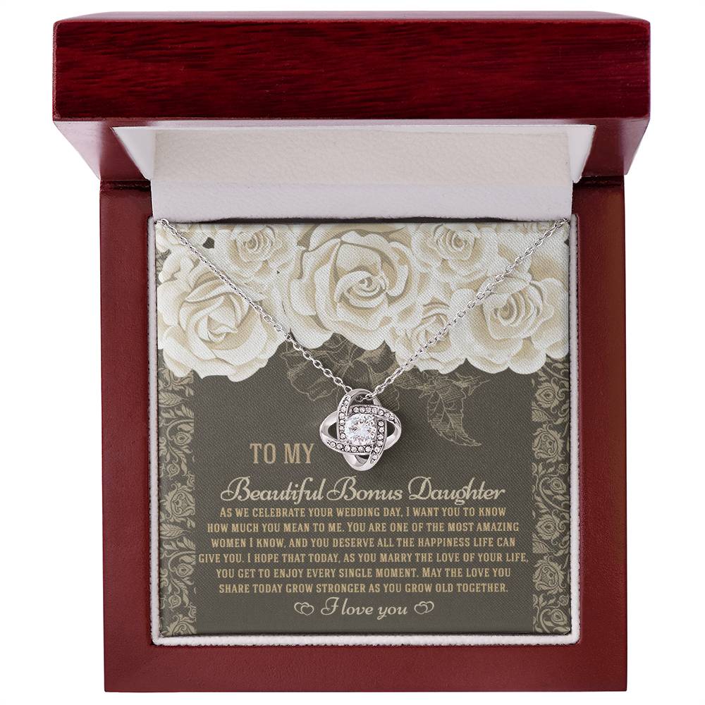 The "To Bonus Daughter, Grow Old Together - Love Knot Necklace" features a gold finish and sparkling cubic zirconia crystals. It comes packaged in a gift box decorated with an ornate floral design and includes a heartfelt message for your daughter on her wedding day.