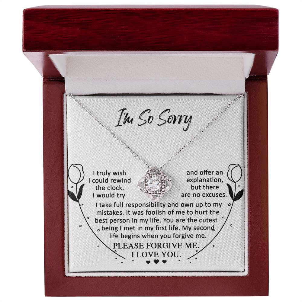 An open jewelry box displaying the Sorry-My First Life - Love Knot Necklace adorned with shimmering cubic zirconia crystals. The text on the box's interior reads an apology note expressing love and a plea for forgiveness, symbolizing an unbreakable bond.