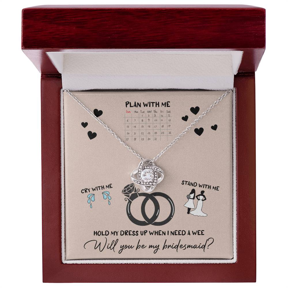 A To Bridesmaid, Will You Be 2 - Love Knot Necklace, adorned with cubic zirconia crystals, is displayed on a card featuring a calendar, wedding rings, and bridesmaid-related illustrations. The text reads, "Will you be my bridesmaid?" Choose from a white gold or yellow gold finish to make the moment even more special.