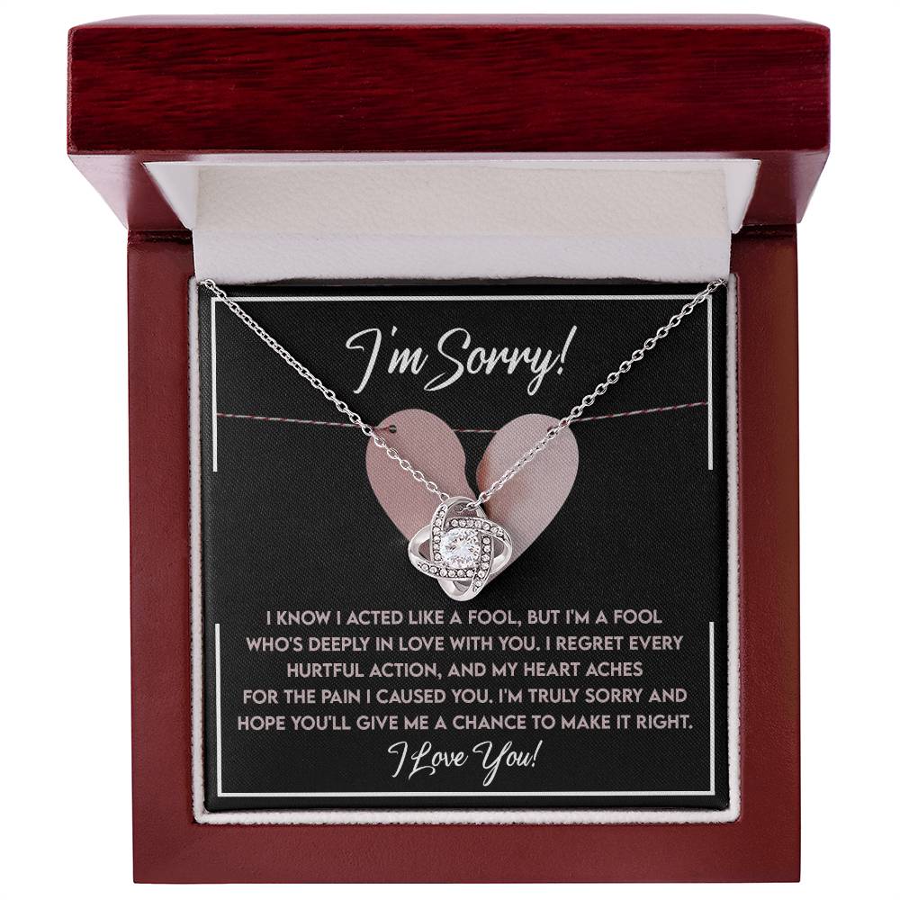 A jewelry box with an open lid reveals the Sorry-Deeply In Love - Love Knot Necklace, adorned with cubic zirconia crystals and a card that reads, "I'm Sorry!" followed by a heartfelt apology message and ending with "I love you!