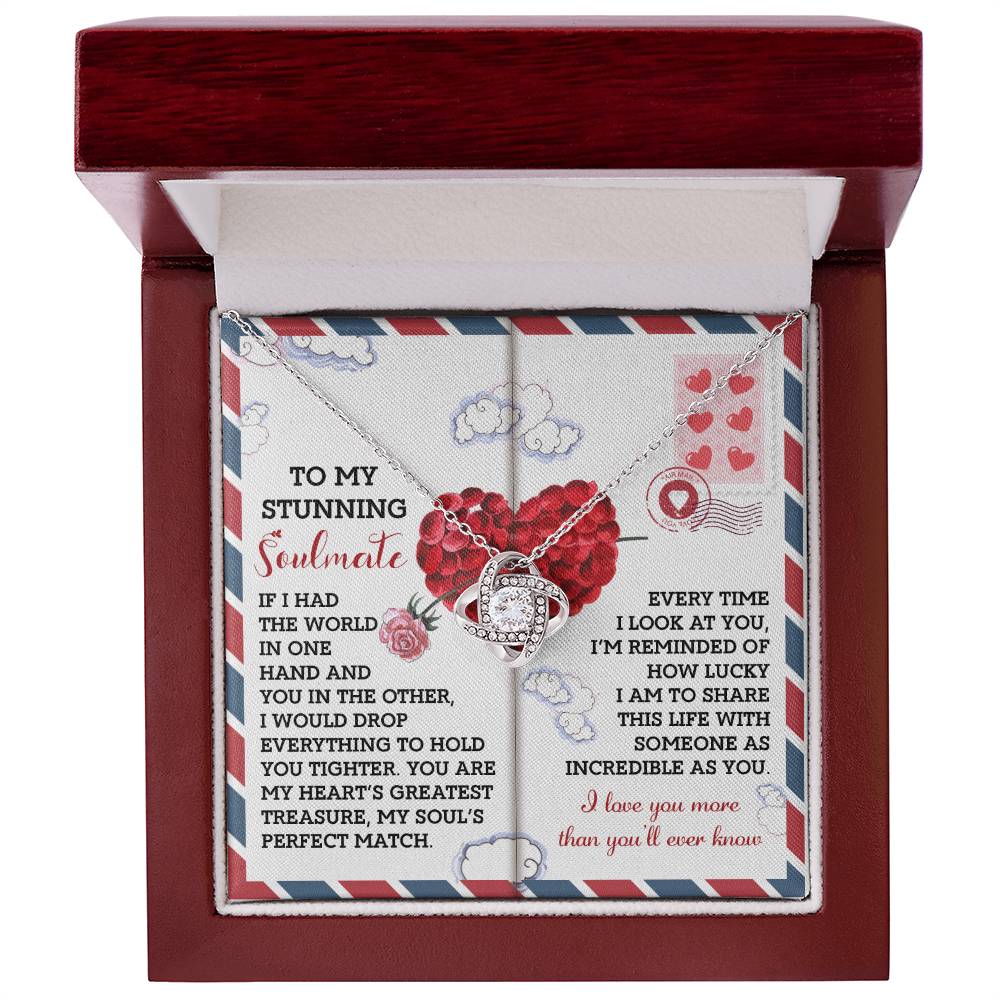 The Soulmate-Perfect Match Love Knot Necklace, featuring interlocking rings adorned with cubic zirconia, is displayed in a box. The backdrop has a heartfelt message on airmail-style paper with heart and cloud designs, creating an ideal personalized gift for expressing love and appreciation.