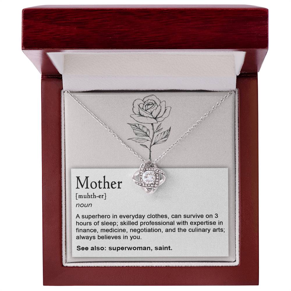 The "To Mom, Superhero - Love Knot Necklace," featuring a circular pendant adorned with cubic zirconia crystals and a stunning white gold finish, is showcased in an open wooden box. Inside the lid is a touching printed message that defines "Mother" as a skilled and tirelessly supportive individual, perfectly capturing the elegance and love embodied by the necklace.