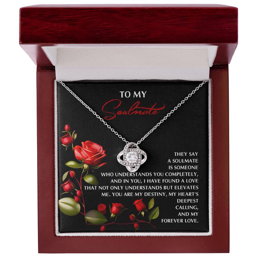 The Soulmate-Deepest Calling Love Knot Necklace, adorned with sparkling cubic zirconia, sits in an open wooden box. The plaque reads "To my soulmate," alongside a romantic message with a red rose illustration—an ideal gift for your loved one.