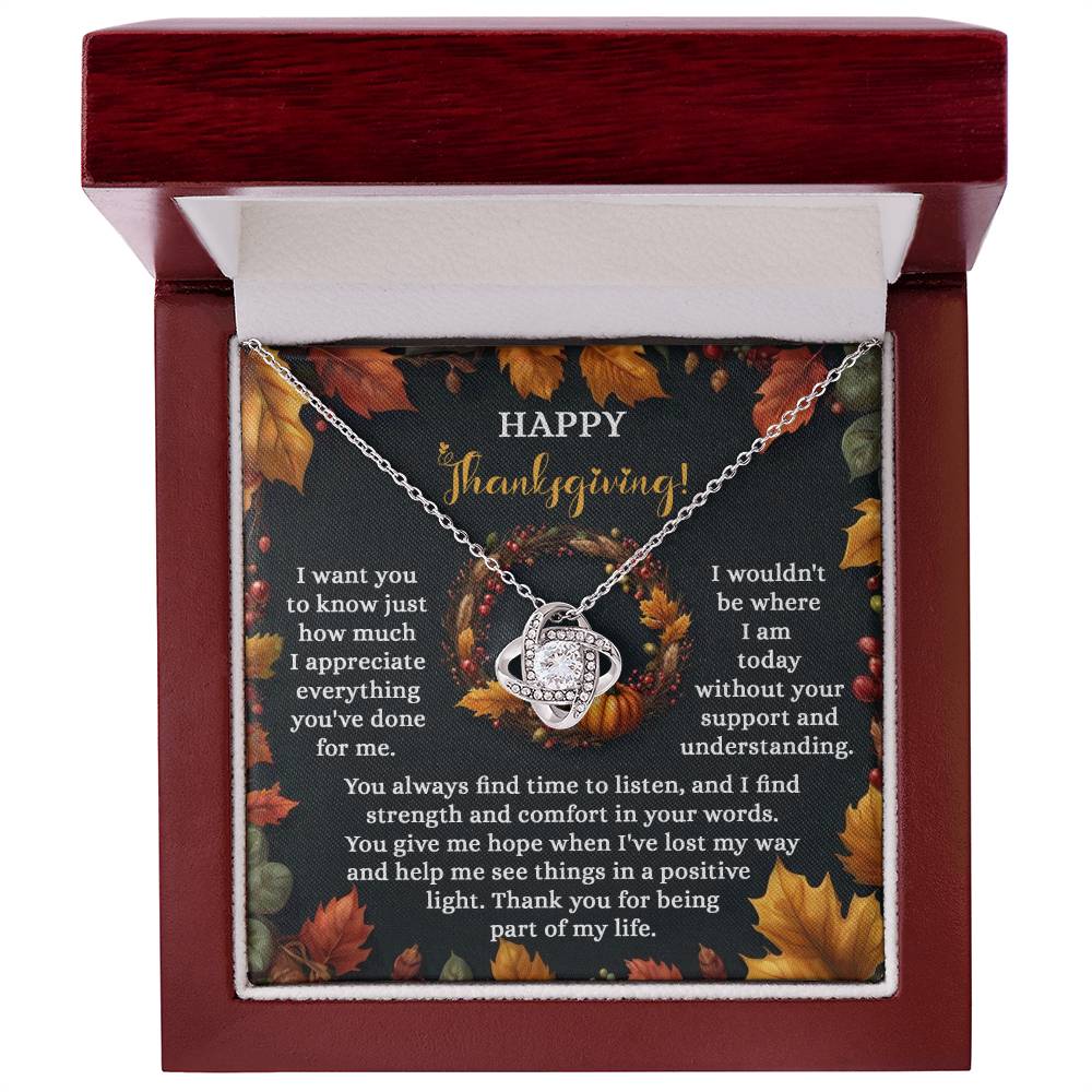 The sophisticated Thanksgiving-Lost My Way - Love Knot Necklace, featuring a striking white gold finish and embellished with cubic zirconia crystals, is presented in a red box. A card adorned with the words "Happy Thanksgiving" is nestled among autumn leaves, conveying a sincere message of gratitude.