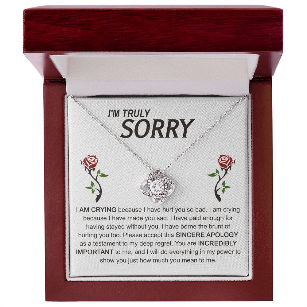 The Sorry-Made You Sad - Love Knot Necklace, crafted in silver with an interlocking design, is presented on a card featuring an apology message and accompanied by two red roses. The text conveys profound regret and vows to make things right, while the cubic zirconia crystals enhance the elegance of this heartfelt gesture.