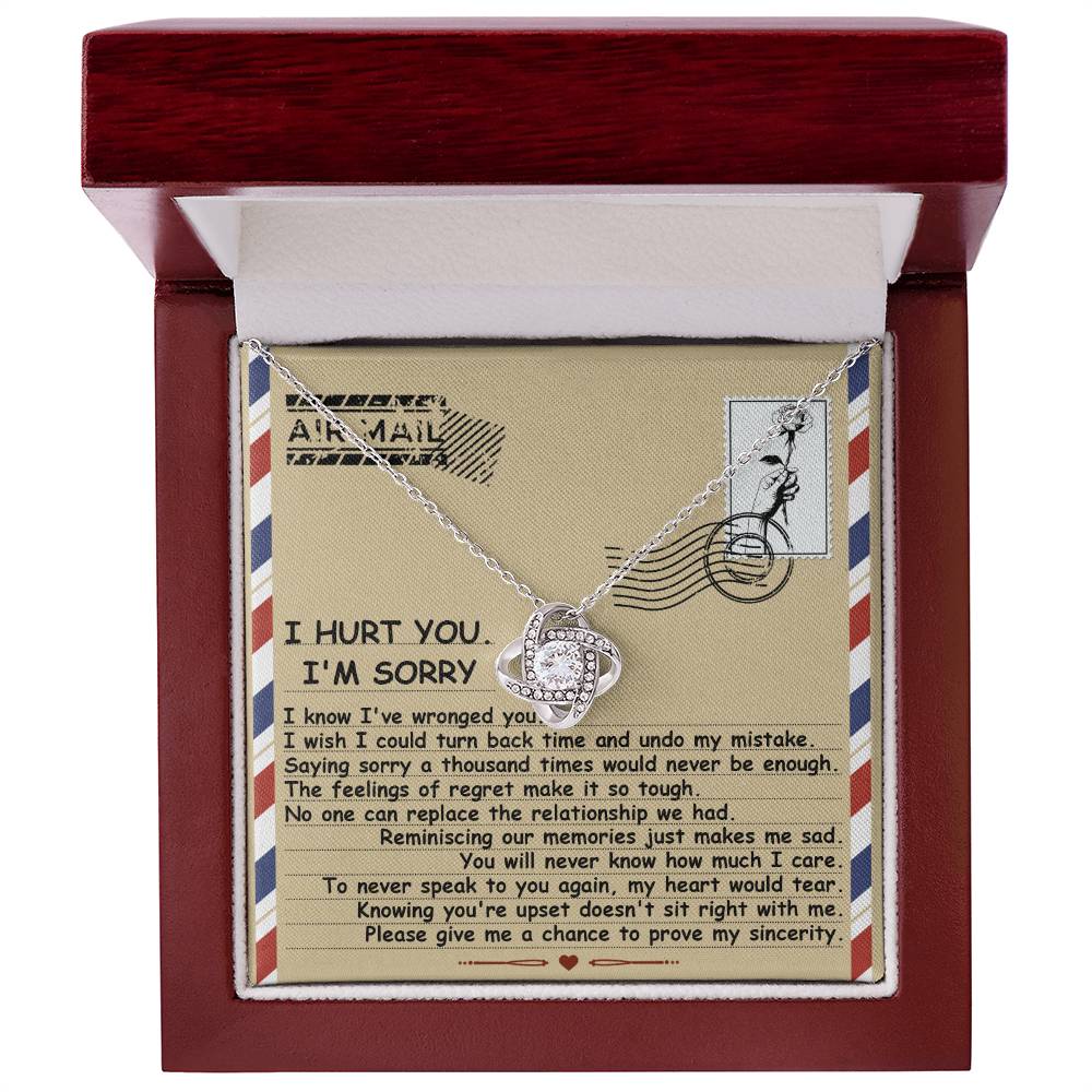 The Sorry-Makes Me Sad - Love Knot Necklace comes in a box and features a heart-shaped pendant adorned with cubic zirconia crystals set in a stunning gold finish. It includes an envelope-themed note expressing regret and asking for forgiveness, complete with heartfelt text and an "Air Mail" graphic at the top.