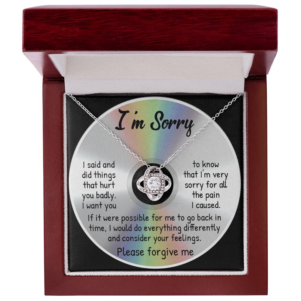 A jewelry box containing the Sorry-Back In Time - Love Knot Necklace, crafted in 14k white gold and adorned with cubic zirconia crystals. The background features a written apology that reads, "I'm Sorry," followed by a heartfelt message asking for forgiveness.