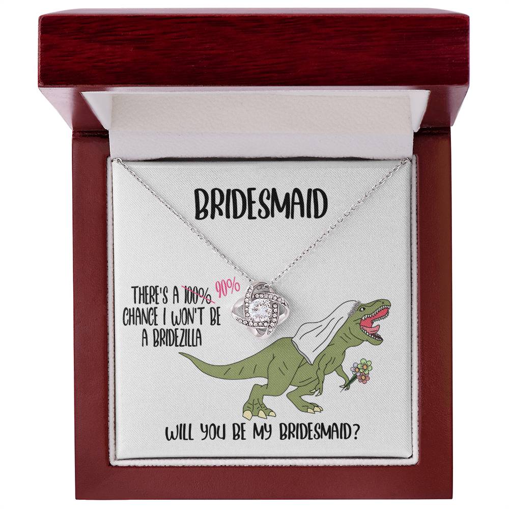 A bridesmaid proposal necklace box featuring a dinosaur with a veil and a stunning To Bridesmaid, Will You Be - Love Knot Necklace in white gold. The text reads, "There's a 90% chance I won't be a bridezilla. Will you be my bridesmaid?