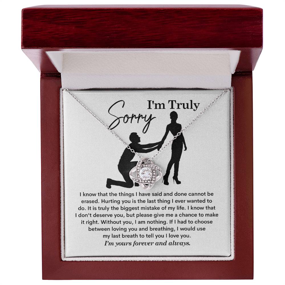 The Sorry-My Last Breath - Love Knot Necklace, a silver piece featuring an intertwined heart pendant decorated with cubic zirconia crystals, is presented on a card. The card includes an apology note with the phrase "I'm Truly Sorry" and the silhouette of one person kneeling before another.