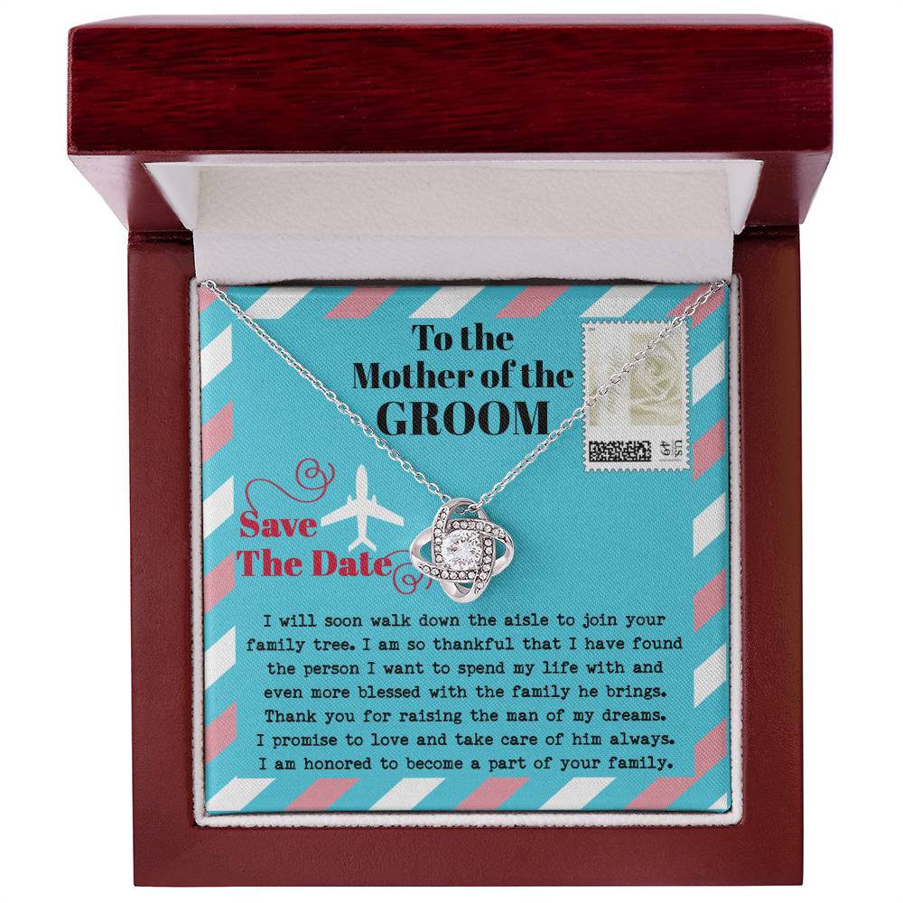 A silver *To Mom Of Groom, Down The Aisle - Love Knot Necklace* with a diamond knot pendant is displayed in a gift box. Adorned with cubic zirconia crystals, the necklace radiates elegance. The box has a message to the "Mother of the Groom" expressing gratitude and a commitment to caring for her son.