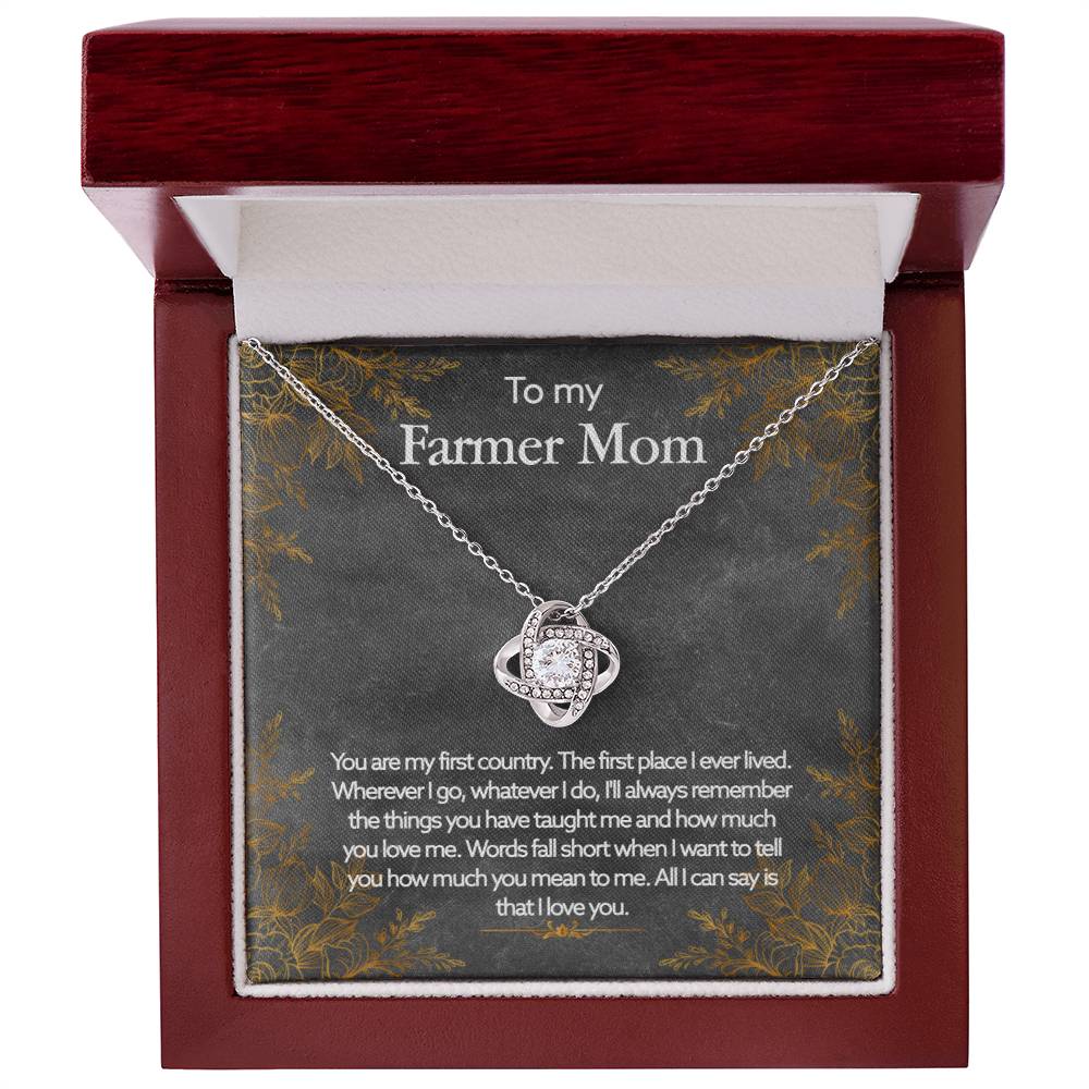 A ShineOn Fulfillment To My Farmer Mom, You Are My First Country - Love Knot Necklace with a heart-shaped pendant, adorned in Cubic Zirconia Crystals, is displayed inside a gift box with an inscription dedicated to a "farmer mom," expressing love and