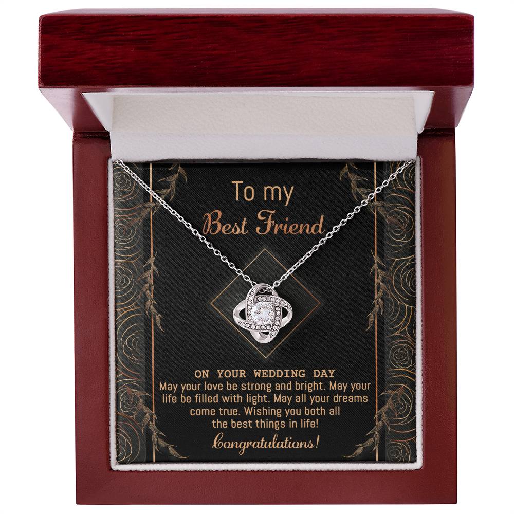 A "To Best Friend Wedding, Strong And Bright - Love Knot Necklace" adorned with cubic zirconia crystals is elegantly displayed on a black card that reads, "To my Best Friend on your wedding day. Congratulations!" The card features a decorative gold border and highlights the necklace's white gold or yellow gold finish options.