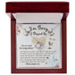 The Sorry-Precious Soul - Love Knot Necklace, featuring an intertwined heart pendant adorned with cubic zirconia crystals, is beautifully displayed in a box. The box comes with an apology note and charming illustrations of flowers, mail stamps, and penguins on a grid-patterned background.