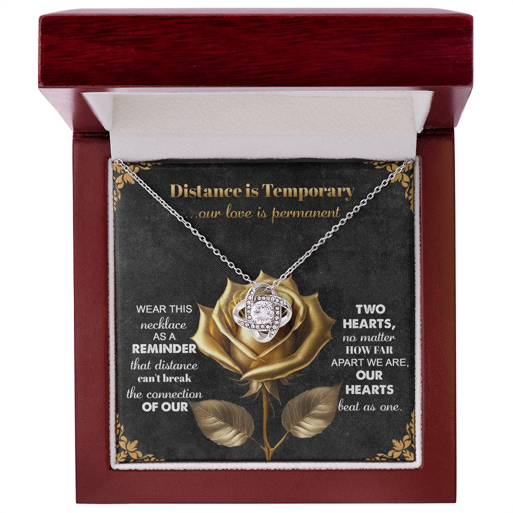 The Soulmate-Love Is Permanent - Love Knot Necklace is presented in an open red box, adorned with a gold rose and cubic zirconia crystals. The card reads: "Distance is Temporary...our love is permanent," making it the perfect gift for your loved one.