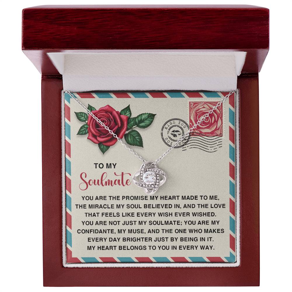 The Soulmate-Made To Me - Love Knot Necklace with intertwined hearts and cubic zirconia crystals sparkles in a jewelry box. The lid shows a heartfelt message to a soulmate, adorned with red roses and postage stamps, making it the perfect personalized gift.