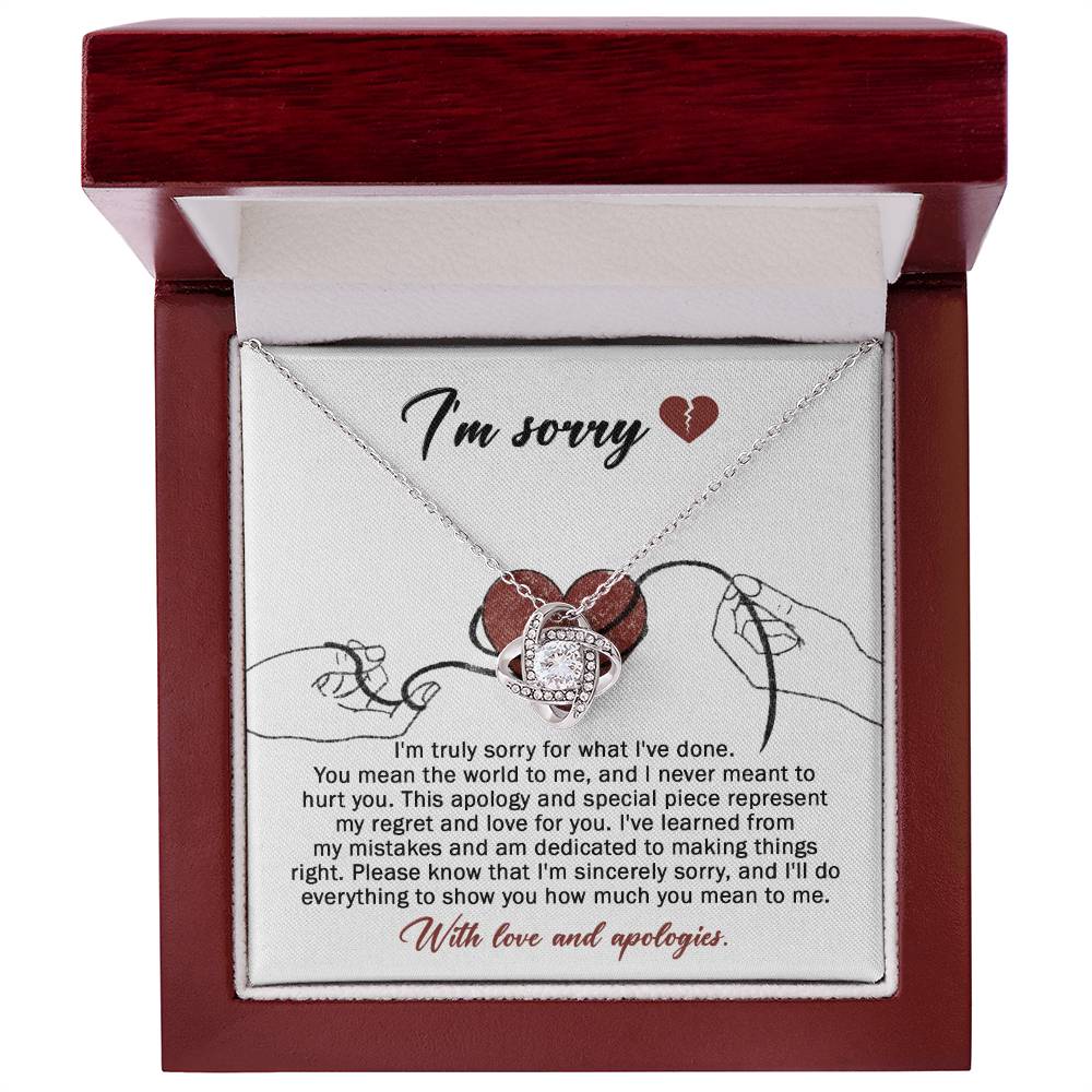 The Sorry-Mean The World - Love Knot Necklace, crafted from white gold and adorned with a heart-shaped pendant, is displayed on a card. This card conveys an apology message expressing regret and dedication to making things right, ending with "With love and apologies." The necklace is embellished with sparkling cubic zirconia crystals that add a touch of elegance.