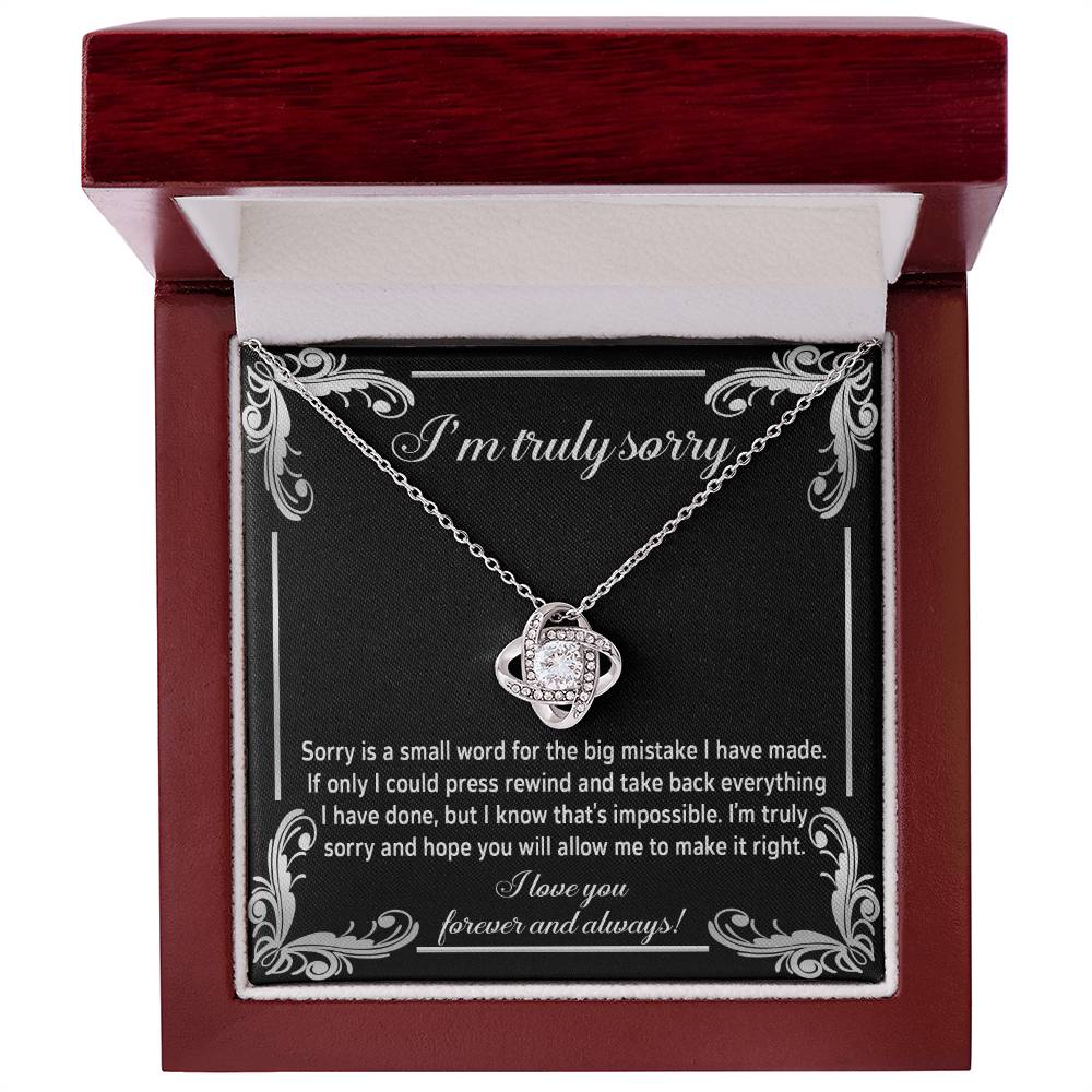 The "Sorry, Make It Right 2 - Love Knot Necklace" showcases a silver interlinked design on a black background. The backdrop features an apology message written in white text, complemented by the brilliance of cubic zirconia crystals.