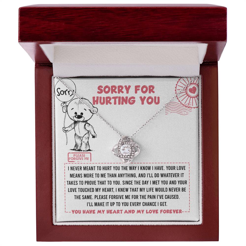 The Sorry-Every Chance - Love Knot Necklace, featuring a heart-shaped pendant adorned with cubic zirconia, is elegantly placed inside an open wooden gift box. The lid of the box showcases a heartfelt apology message accompanied by a drawing of a bear holding a heart.