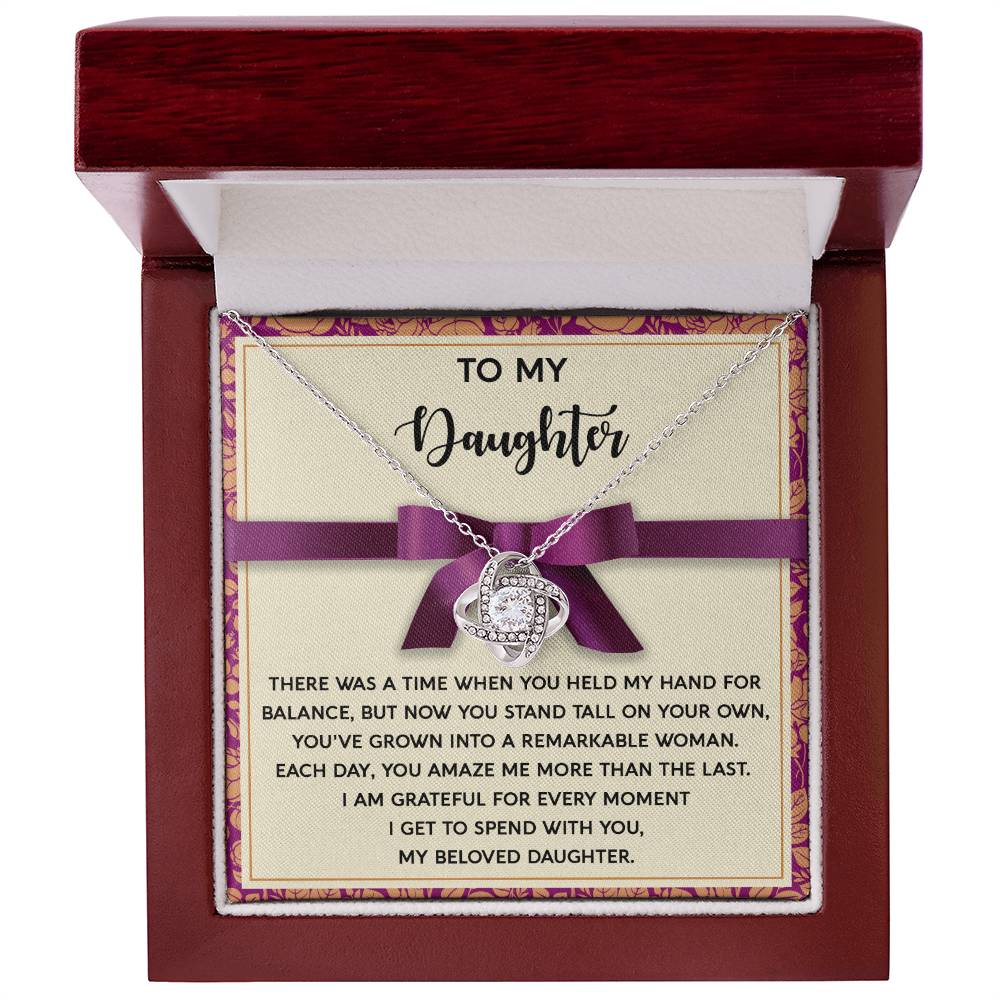 The "Daughter-Spend With You - Love Knot Necklace" comes in a red box with a card that reads, "To my Daughter" and includes a heartfelt message about her growth into a remarkable woman and the joy of sharing moments with her. Adorned with cubic zirconia crystals and available in either white gold or yellow gold finish, it’s a piece she’ll cherish forever.