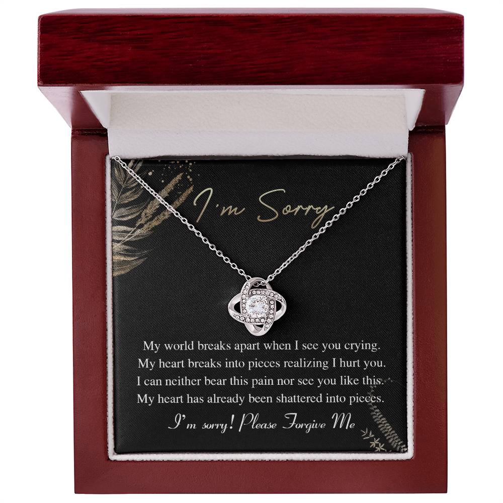 The Sorry-See You Crying - Love Knot Necklace, featuring an intertwined pendant adorned with cubic zirconia crystals, is elegantly displayed on a black card with the inscription "I'm Sorry" and an apology message in white text.