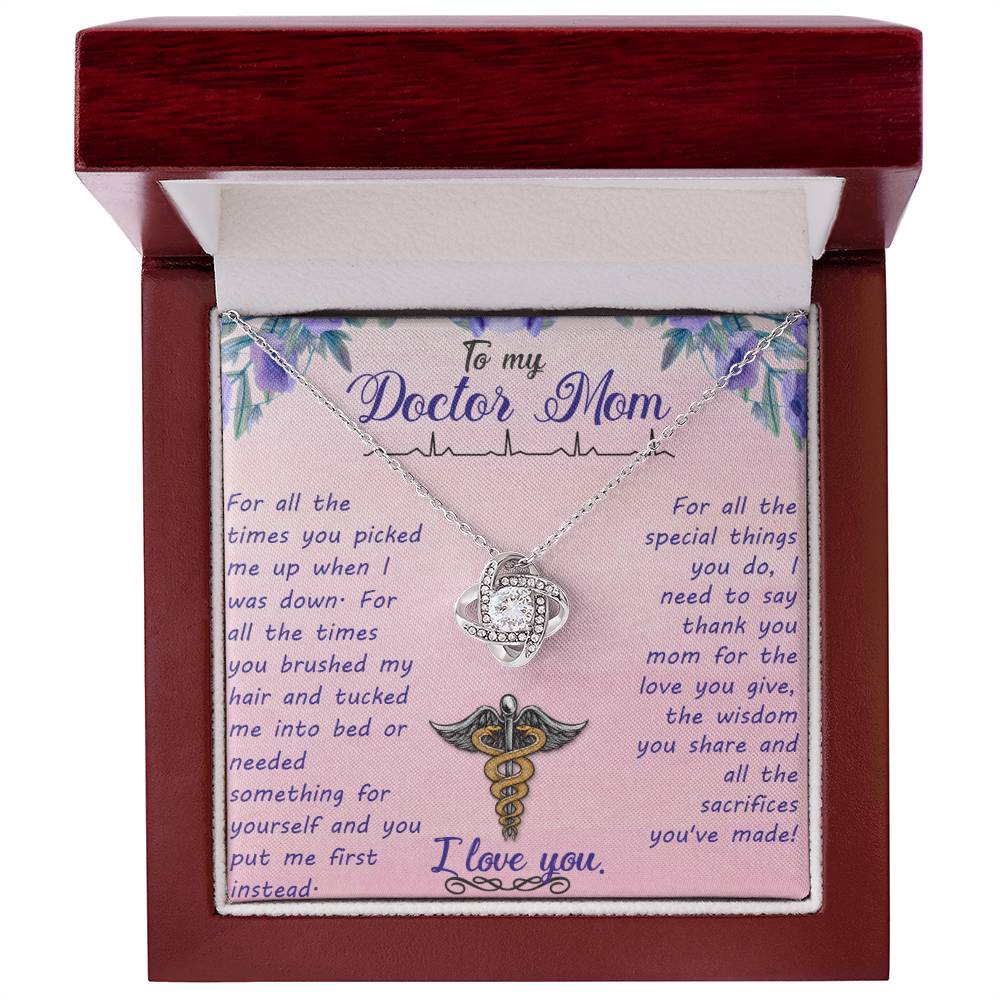 A "To My Doctor Mom, For All The Times You Picked Me Up" Love Knot Necklace with a medical symbol, featuring Cubic Zirconia Crystals, is presented inside a gift box with an appreciative message dedicated to a doctor mom by ShineOn Fulfillment.