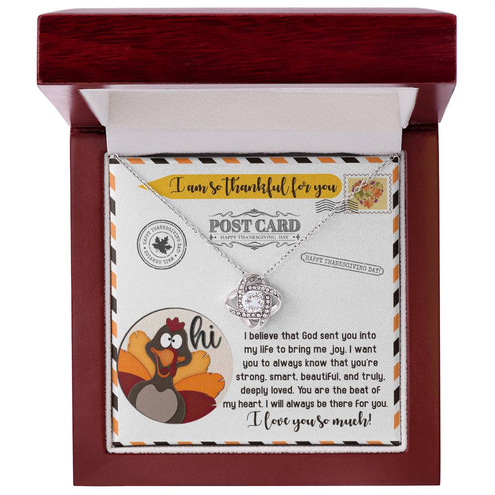 The Thanksgiving-The Beat - Love Knot Necklace, featuring a dazzling cubic zirconia and a sophisticated gold finish, is beautifully presented in a wooden box. It also includes a Thanksgiving-themed card with a turkey illustration and an uplifting message.