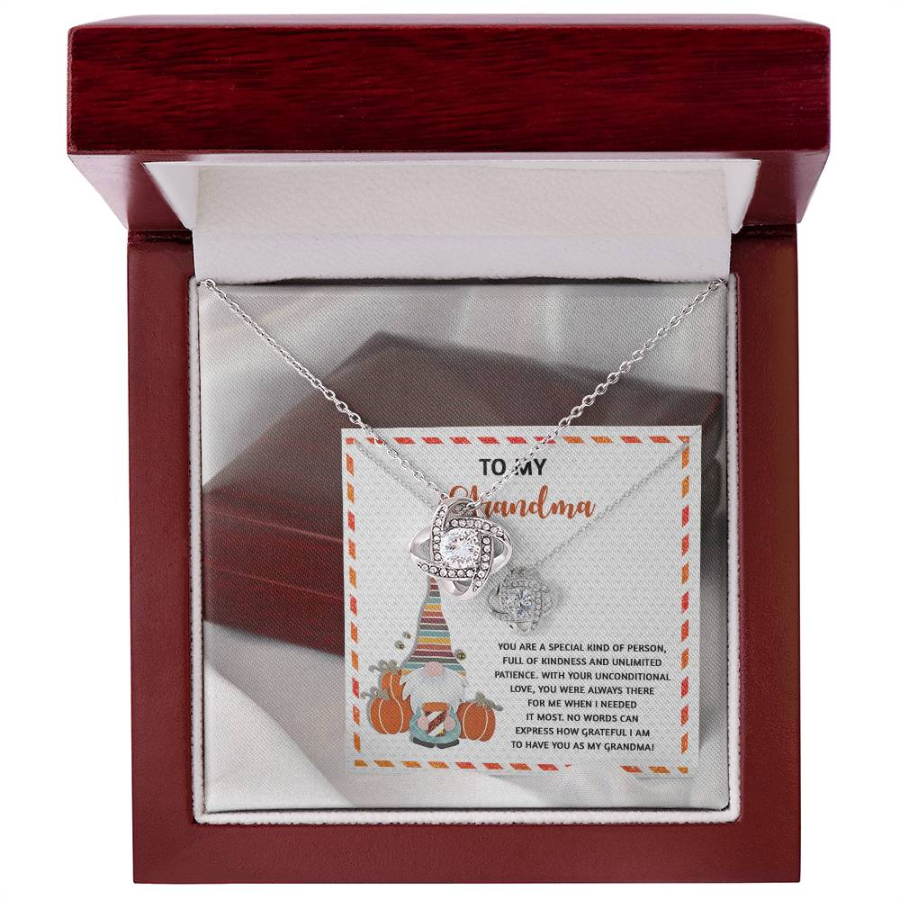 A silver Love Knot Necklace, adorned with sparkling Cubic Zirconia, sits elegantly in an open red jewelry box. The message card inside reads "To My Grandma" for the "Grandma-Needed It Most - Love Knot Necklace.