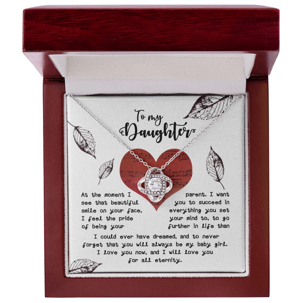 The Daughter-On Your Face - Love Knot Necklace features a heart-shaped pendant beautifully adorned with cubic zirconia crystals, available in either a white gold or yellow gold finish. It comes elegantly packaged in a gift box, which includes a heartfelt message from a parent to their daughter, expressing pride, love, and encouragement amidst decorative hearts and leaves.