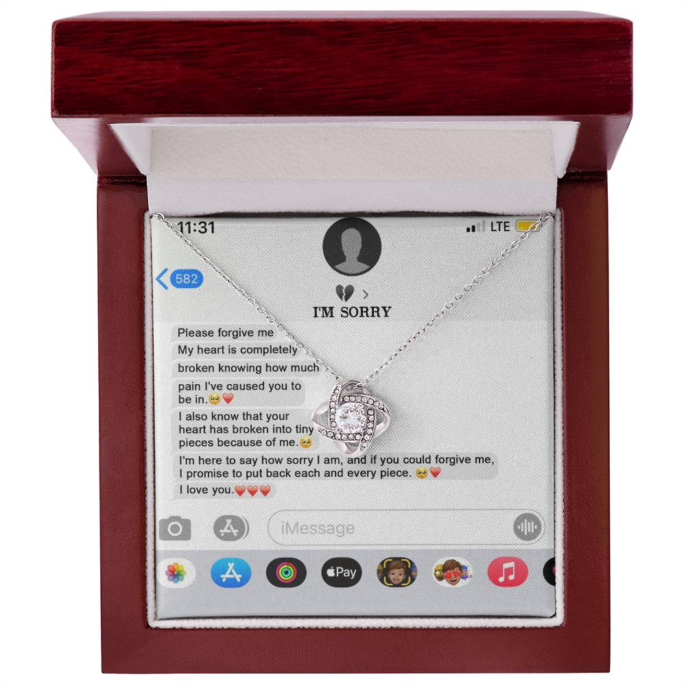 The "Sorry, Completely Broken - Love Knot Necklace" features a gold finish and sparkling cubic zirconia crystals, displayed atop a printed text message conversation that conveys an apology and expresses love.