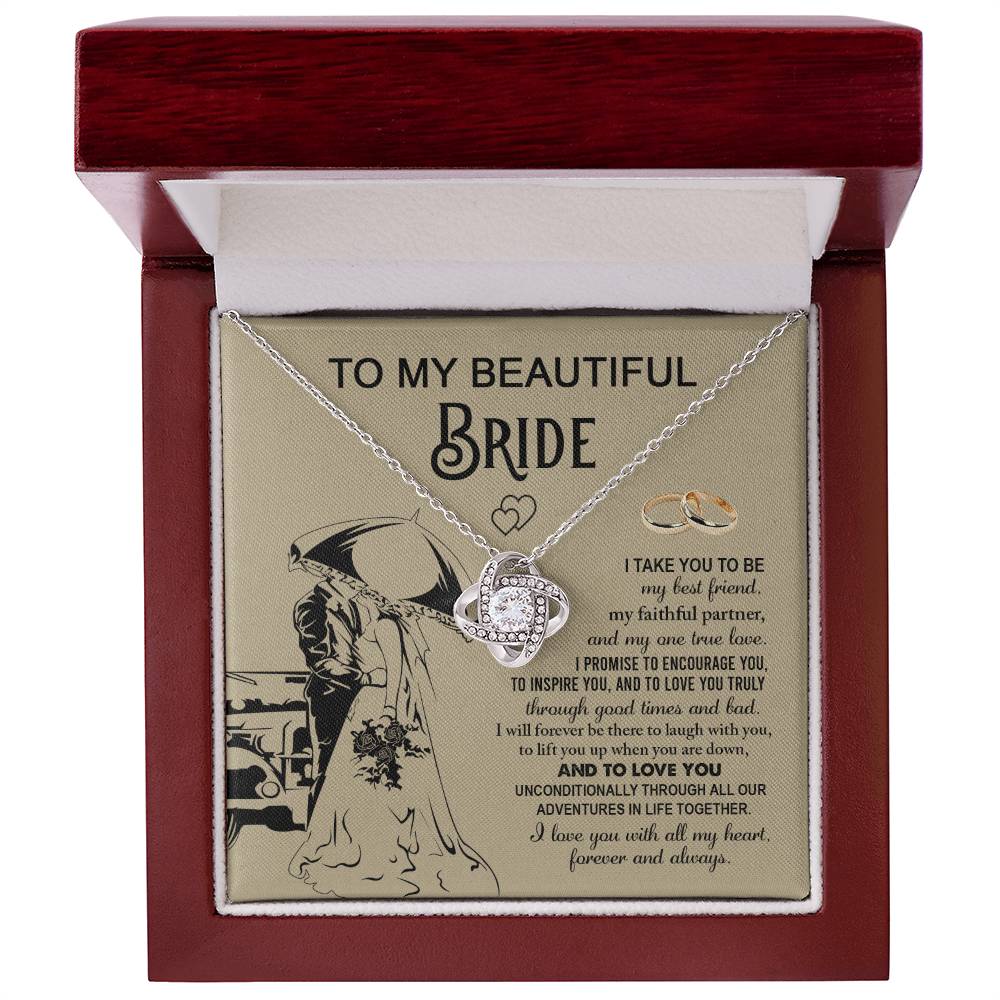 A "To My Bride, Faithful Partner - Love Knot Necklace" adorned with cubic zirconia crystals is displayed in a box. The background features a silhouette of a couple under an umbrella, two rings, and a heartfelt message to a bride, making it the perfect unique gift.