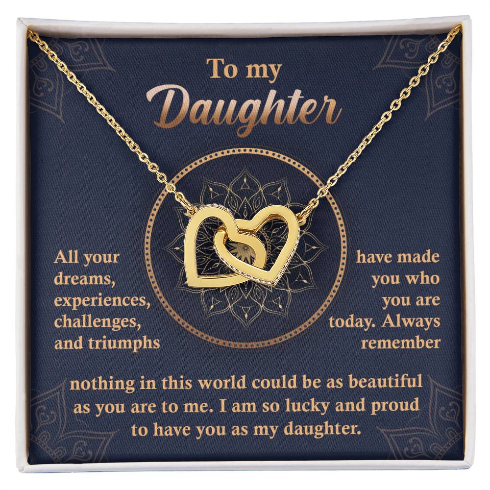 A "To My Daughter, All Your Dreams - Interlocking Hearts Necklace" with a rose gold finish and sparkling cubic zirconia crystals sits in a display box, accompanied by a heartfelt message expressing a parent's pride and love for their daughter.