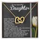 The Daughter-Heart Love necklace, with a rose gold interlocking hearts design and sparkling cubic zirconia crystals, is displayed on a card featuring a heartfelt message to a daughter. It sits elegantly beside a white tulip, symbolizing love and elegance.