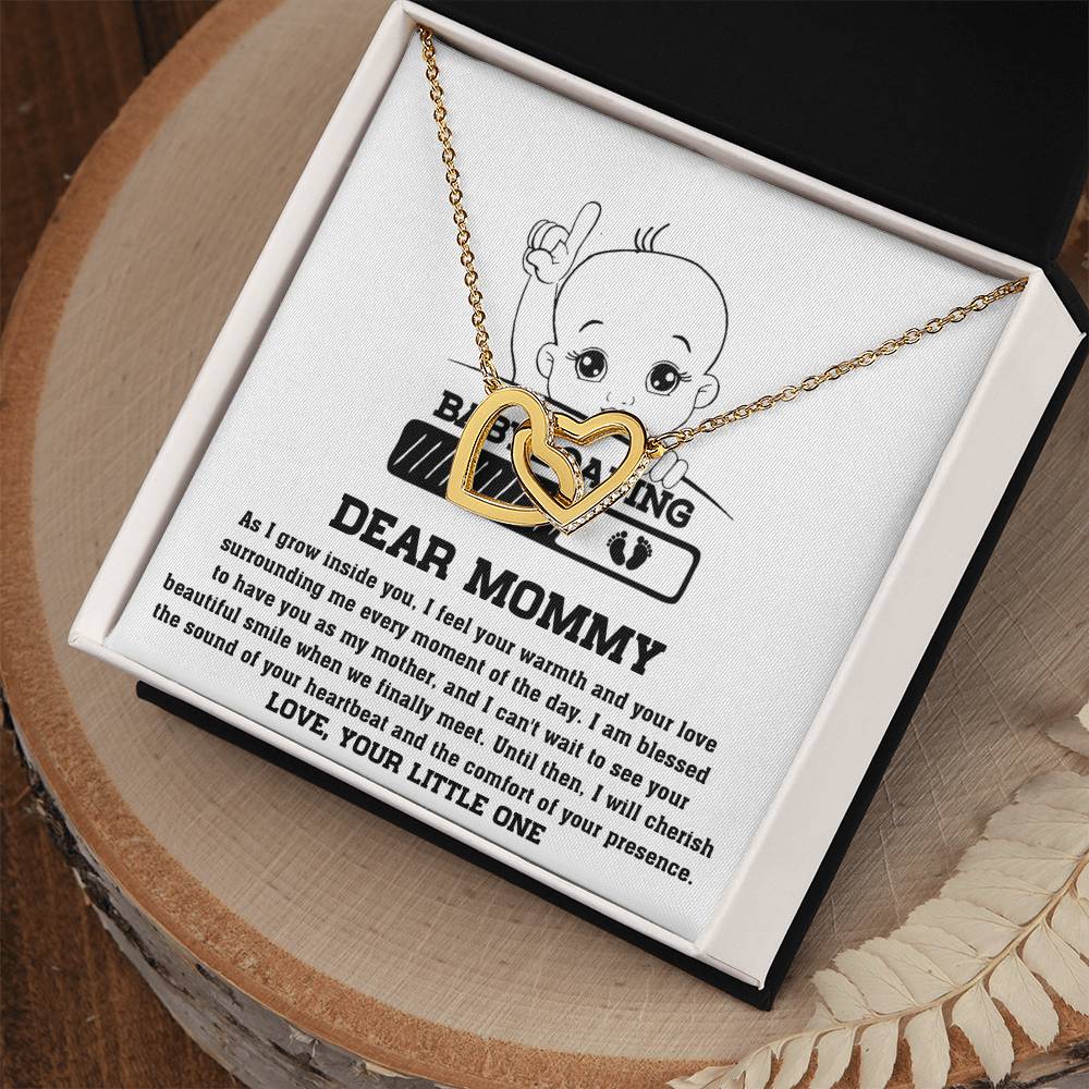 ShineOn Fulfillment's To Mama To Be, Your Little One - Interlocking Hearts Necklace pendant with a mother and child embracing, placed on a box with a printed message to mom from a baby, on a wooden surface.