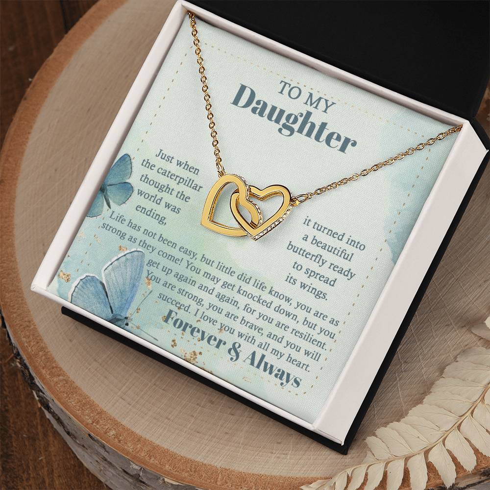 The "To Daughter, Beautiful Butterfly - Interlocking Hearts Necklace" is beautifully presented in a box adorned with blue butterflies and motivational messages about resilience and love. Sparkling with cubic zirconia crystals, this adjustable-length necklace ensures a perfect fit, making it a treasured keepsake for your daughter.