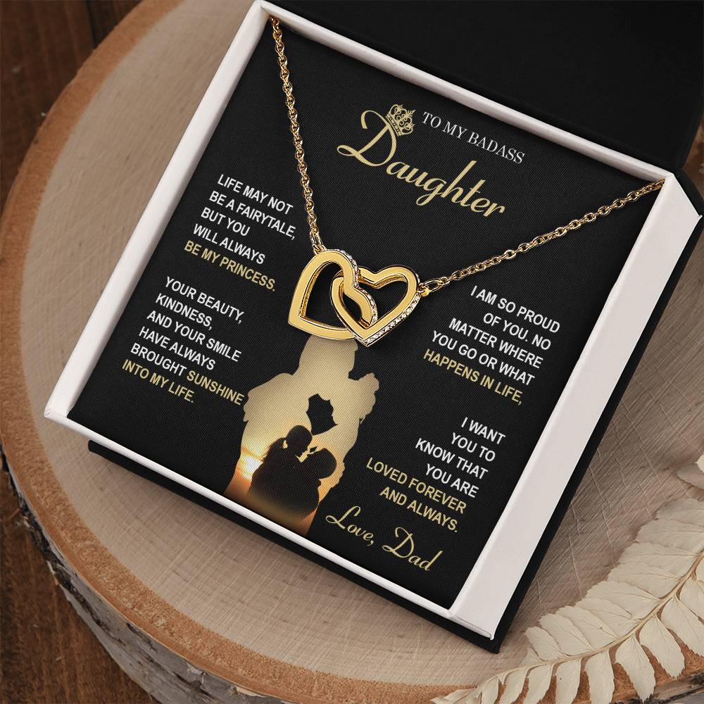 The "To Daughter, Be My Princess - Interlocking Hearts Necklace" with a rose gold finish and adorned with cubic zirconia crystals is displayed in a box that features a heartfelt message from a father to his daughter about love, support, and pride. The text and silhouette of a father and daughter are also included below.