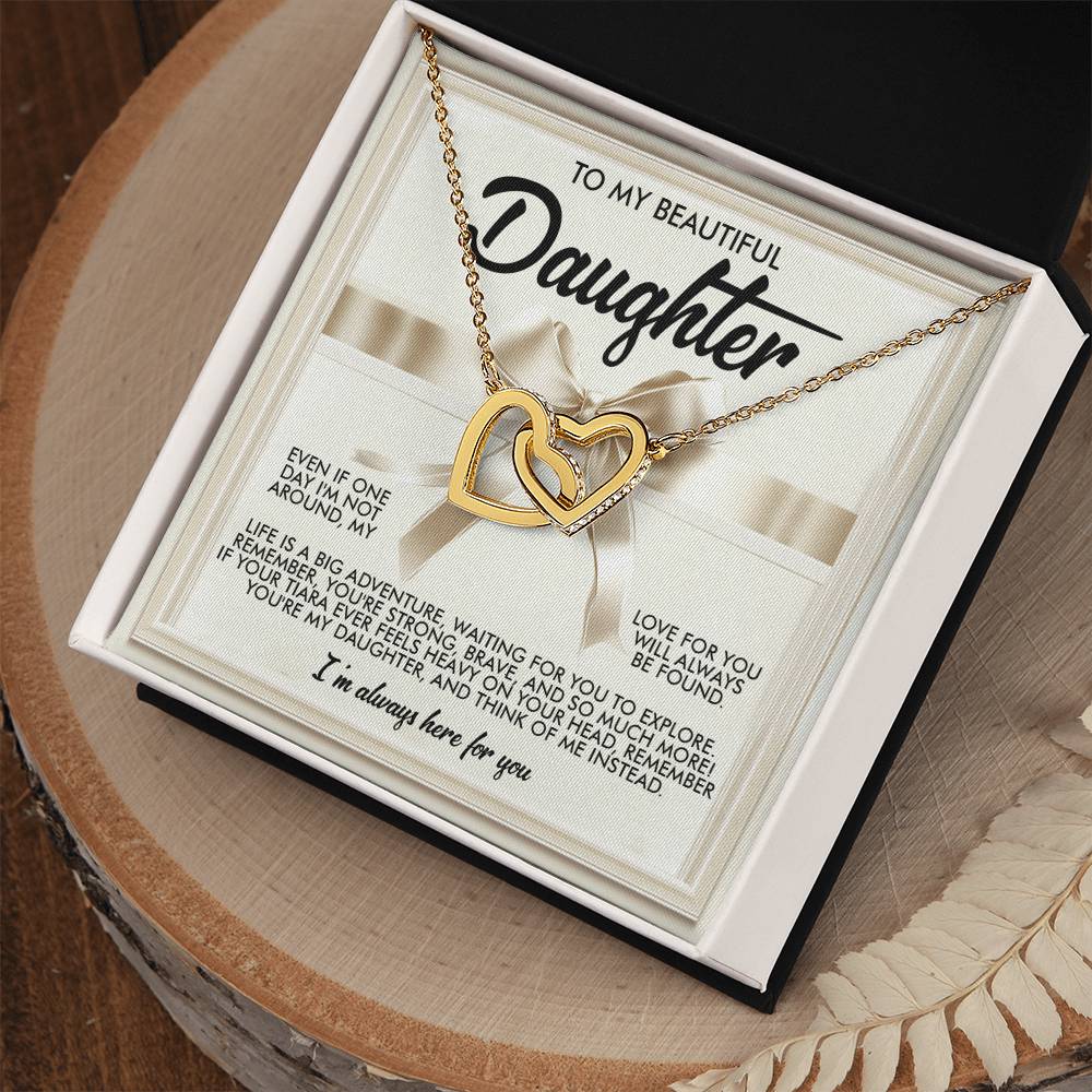 The Daughter-Heavy Tiara Interlocking Hearts Necklace, featuring a rose gold finish and sparkling cubic zirconia crystals, is elegantly displayed in an open white box on a wooden surface. The box includes a heartfelt message for a daughter, expressing love and encouragement.