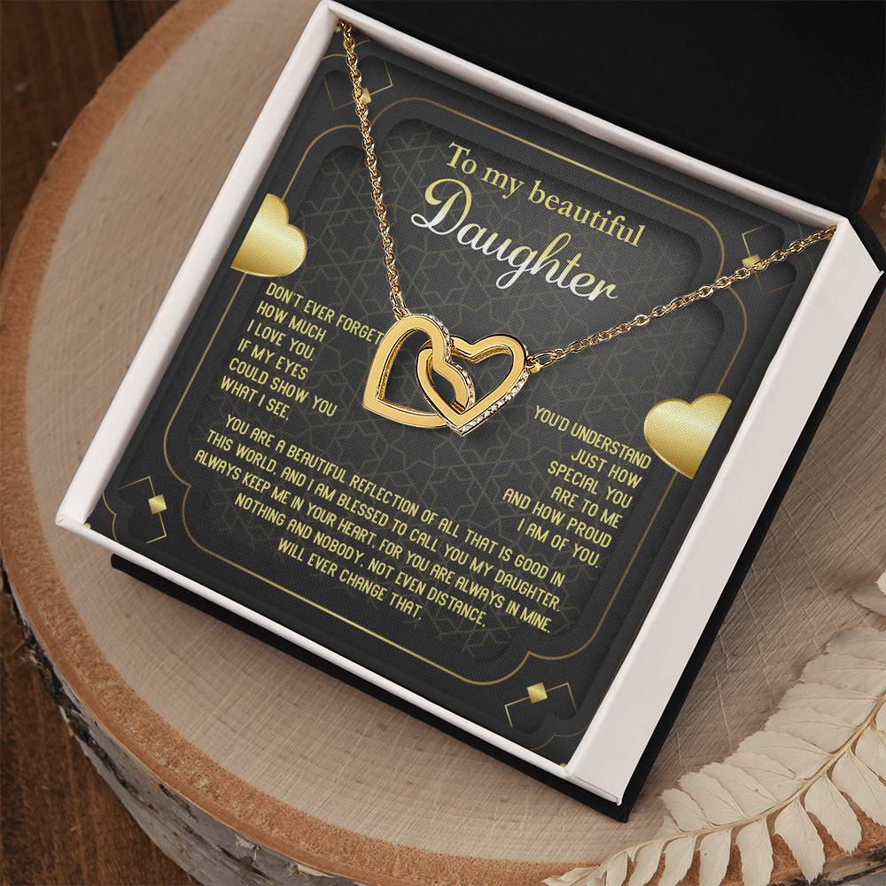 The "To Daughter, Beautiful Reflection - Interlocking Hearts Necklace" features an 18k yellow gold finish and is presented on a card that conveys a heartfelt message of love, pride, and eternal connection. The interlocking hearts are adorned with sparkling cubic zirconia crystals.