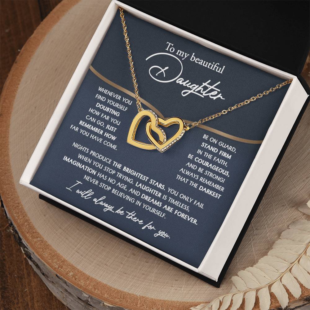 The "To Daughter, Brightest Stars - Interlocking Hearts Necklace," crafted from high-quality polished surgical steel and adorned with cubic zirconia crystals, is presented on a message card addressed to a daughter, offering encouraging and motivational words.