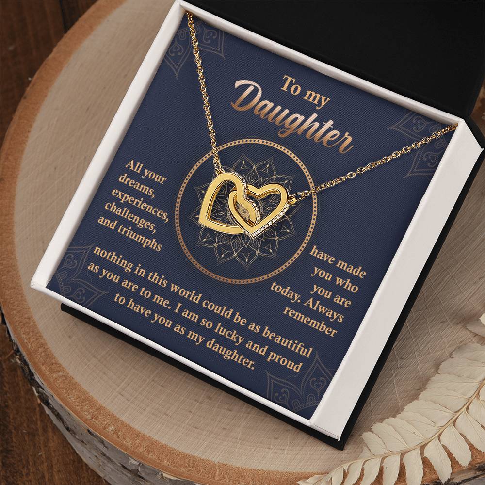 A "To My Daughter, All Your Dreams - Interlocking Hearts Necklace" with a rose gold finish and sparkling cubic zirconia crystals sits in a display box, accompanied by a heartfelt message expressing a parent's pride and love for their daughter.