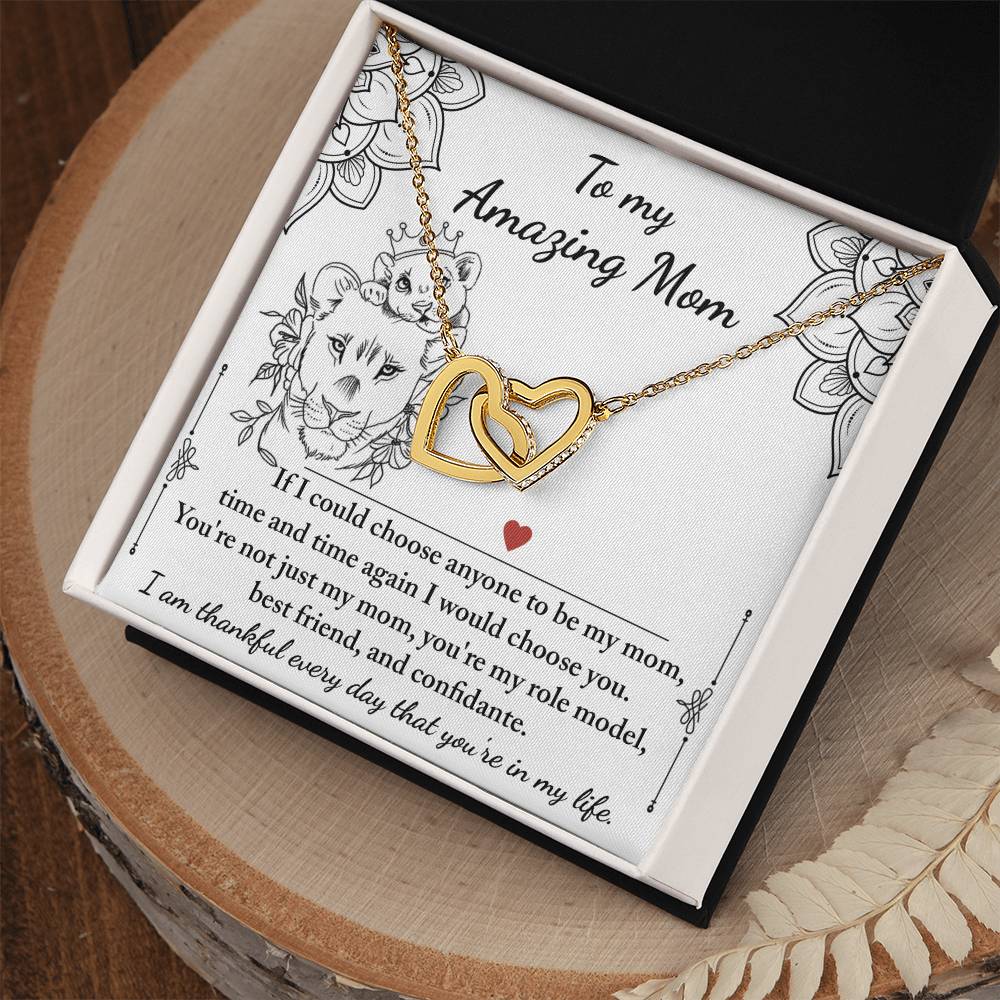 The "To Mom, Be My Mom" Interlocking Hearts Necklace features gold intertwined hearts on a card with "Amazing Mom," enhanced by a lion illustration and red heart. Adorned with cubic zirconia crystals, it’s a unique gift she'll cherish forever.