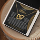 The Mom-Best Friend - Interlocking Hearts Necklace, adorned with cubic zirconia crystals in a rose gold finish, rests elegantly in a box with a heartfelt message of gratitude and love for a mother. Set against a black background with gold accents, it graces a wooden surface beautifully.