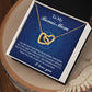 The jewelry box contains an "Interlocking Hearts Necklace" with cubic zirconia crystals. The lid, inscribed with "To My Bonus Mom," carries a heartfelt message of gratitude and love. The elegant piece is placed on a wooden surface beside a white feather. Product: Bonus Mom-I Needed You - Interlocking Hearts Necklace.