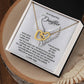 A stunning necklace, "Daughter-An Angel - Interlocking Hearts," with a gold heart design and cubic zirconia crystals is presented in a jewelry box. The background has a heartfelt message to a daughter about their love and bond. The open box sits on a wooden surface.