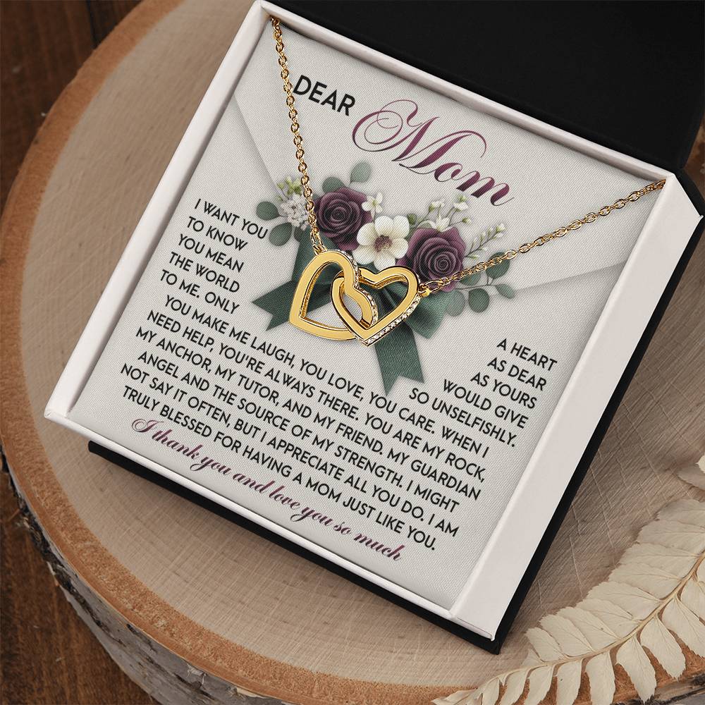 A Mom-Guardian Angel gift box showcases an Interlocking Hearts Necklace with a rose gold finish, each heart sparkling with cubic zirconia crystals. Behind the necklace is a heartfelt message to "Dear Mom" expressing love and gratitude, all beautifully presented on a wooden surface.