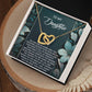 The Daughter-Happiest Person - Interlocking Hearts Necklace features a gold heart in an 18k yellow gold finish with cubic zirconia crystals. It comes in a black box with a floral card saying "To My Daughter," symbolizing love and connection.