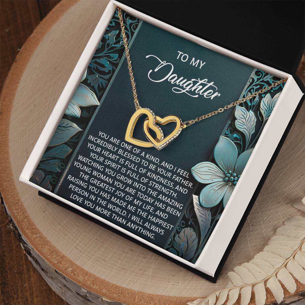 The Daughter-Happiest Person - Interlocking Hearts Necklace features a gold heart in an 18k yellow gold finish with cubic zirconia crystals. It comes in a black box with a floral card saying "To My Daughter," symbolizing love and connection.