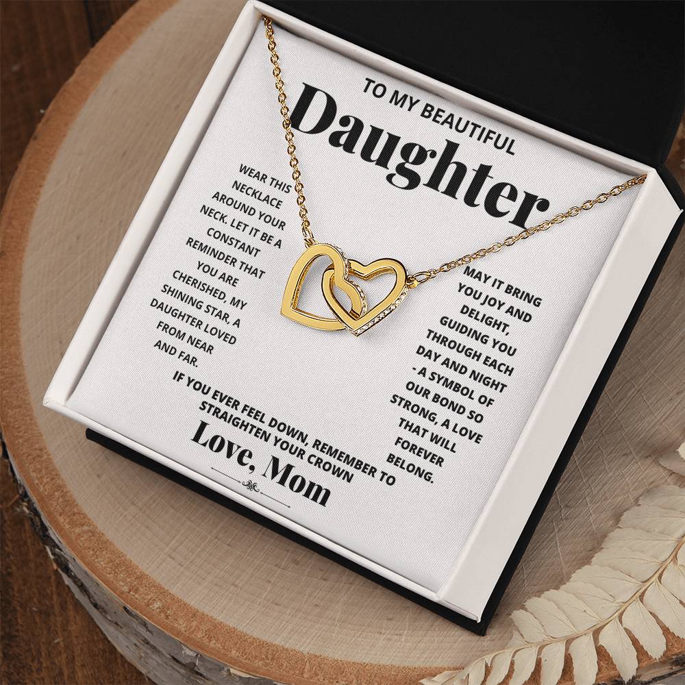 A "To My Daughter, Wear This Necklace - Interlocking Hearts Necklace" with interlocking heart pendants adorned with cubic zirconia crystals on a printed message card from a mother to her daughter, expressing love and encouragement.